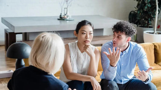 Couple in therapy session discussing relationship, seated on yellow couch with counselor