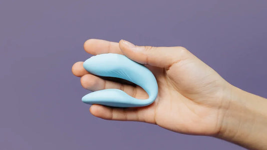 Hand holding light blue curved adult toy for intimate pleasure