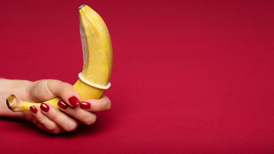 Hand holding banana with condom on red background