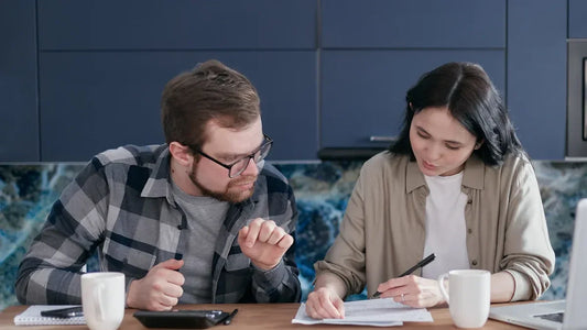 Couple reviewing documents at kitchen table with coffee and laptop