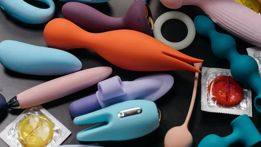 Colorful vibrators, silicone toys, and condoms arranged on dark surface for adult pleasure