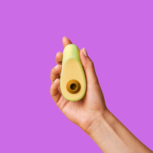 Avocado-shaped personal massager held in hand against purple background